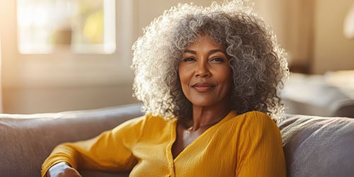 Older black woman relaxing on couch in sunlit living room captur